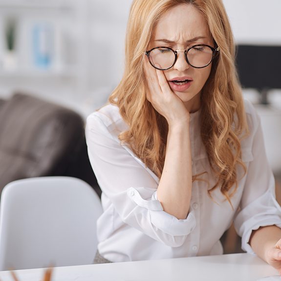 Woman with glasses sitting at table with tooth pain